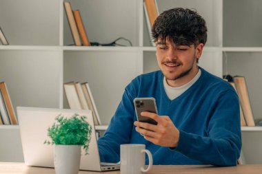 Masasında cep telefonu ve dizüstü bilgisayarı olan genç bir öğrenci.