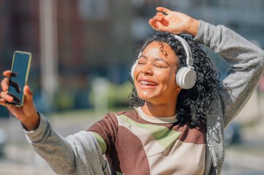 Afro saçlı, kulaklıklı ve cep telefonlu Latin bir kız.