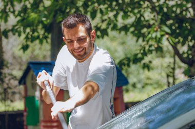 Adam arabayı ya da dışarıdaki arabayı yıkıyor.