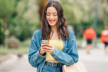 Kız sokakta cep telefonuyla yürüyor.