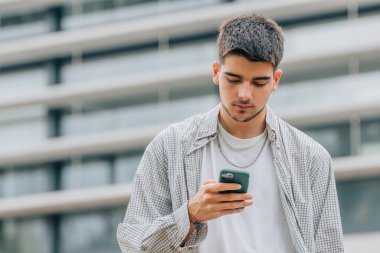 Sokaktaki genç adam cep telefonuna ya da akıllı telefona bakıyor.