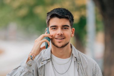 Genç adam cep telefonuyla konuşuyor. Kameraya bakıyor.