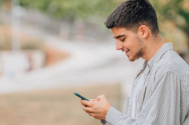 Sokaktaki genç adam cep telefonuna bakıyor.