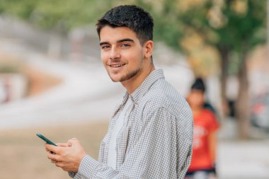 Sokaktaki genç adam cep telefonuna bakıyor.