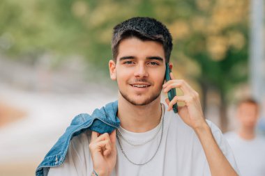 Sokaktaki genç adam cep telefonu ya da akıllı telefonuyla konuşuyor.