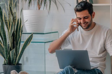 Evde bilgisayar ve cep telefonu olan genç bir adam.