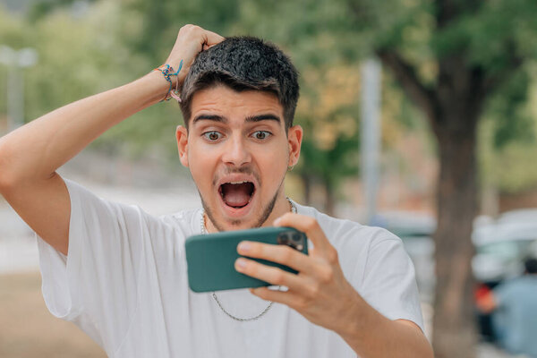 испуганный или удивленный молодой человек или студент, глядя на мобильный телефон