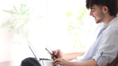 Dizüstü bilgisayarı ve cep telefonu olan genç bir adam.