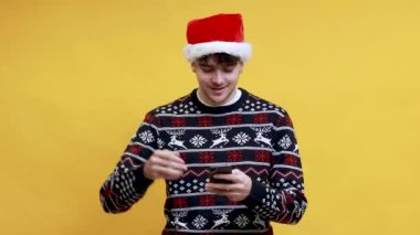 Kafkasyalı genç adam Noel Baba şapkası takıyor. Arka planda izole edilmiş başarılı bir ifadeyle cep telefonuyla yazı yazıyor.