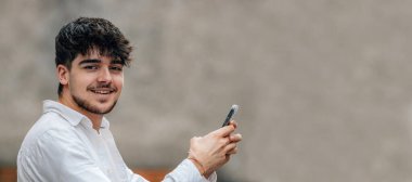 Genç erkek sokakta cep telefonuna ya da akıllı telefona bakıyor.