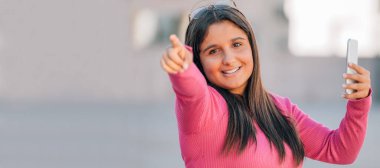 Sokakta kameraya çevrilmiş cep telefonu olan genç bir kız ya da öğrenci.