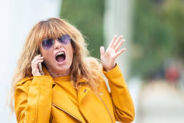 Cep telefonuyla konuşan orta yaşlı bir kadın korkmuş ya da şok olmuş.