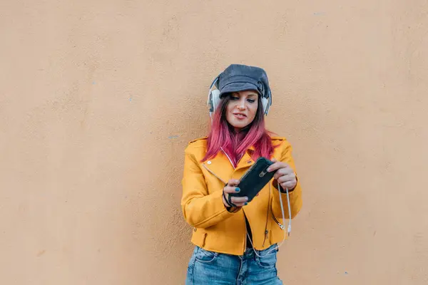 ストリートウォールで隔離された携帯電話とイヤホンを持つ都市の少女 ストック写真