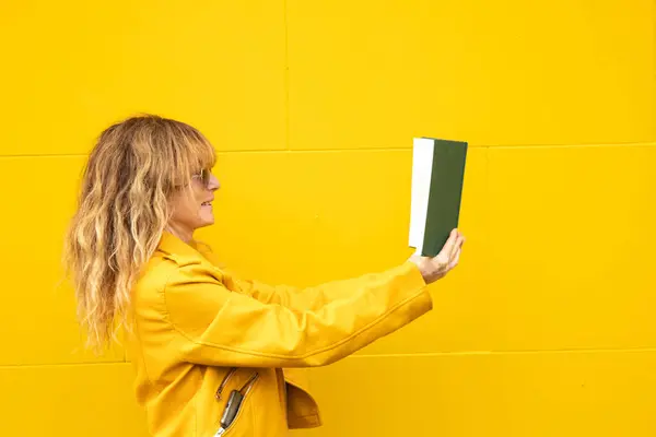 黄色い壁の背景にある教科書を持つ女性 ロイヤリティフリーのストック写真