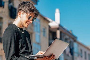 Dışarıda dizüstü bilgisayarı olan genç adam.