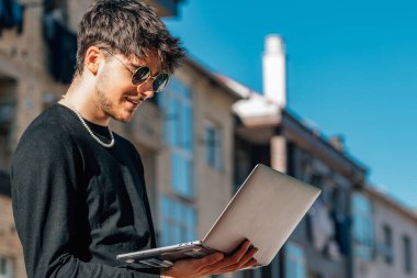 Dışarıda dizüstü bilgisayarı olan genç adam.