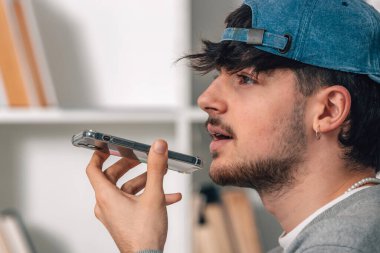 Şapkalı ve telefonlu genç adam sesli mesaj gönderiyor.