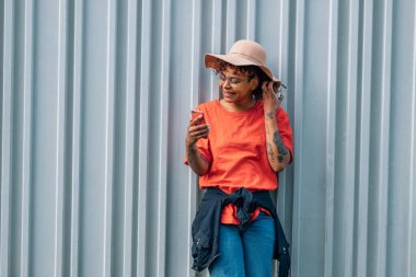 african american girl with hat isolated on street wall with mobile phone