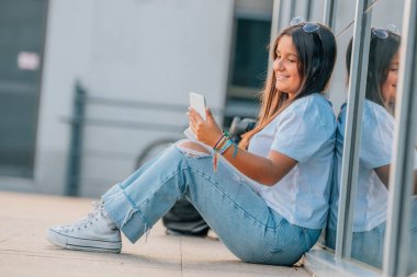 Okulda cep telefonu, sırt çantası ve kitapları olan bir öğrenci