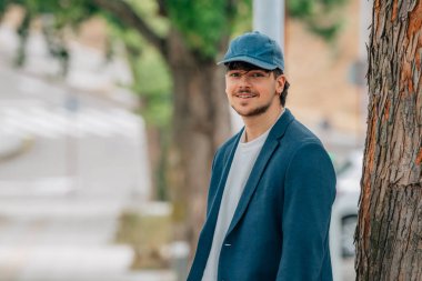 Takım elbiseli ve şapkalı bir öğrenci gülümsüyor.