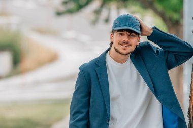 Takım elbiseli ve şapkalı bir öğrenci gülümsüyor.