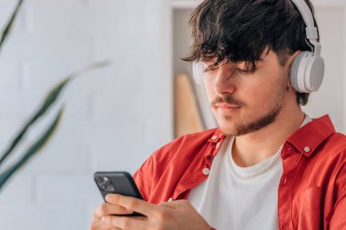 Kulaklık ve cep telefonu olan genç bir erkek portresi.