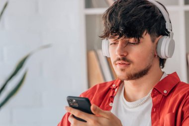 Kulaklık ve cep telefonu olan genç bir erkek portresi.