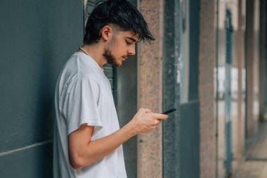 Genç adam caddede cep telefonuna bakıyor.