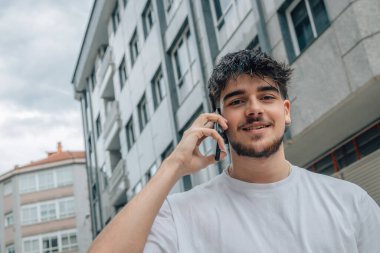 Sokaktaki genç adam cep telefonu ya da akıllı telefonuyla konuşuyor.