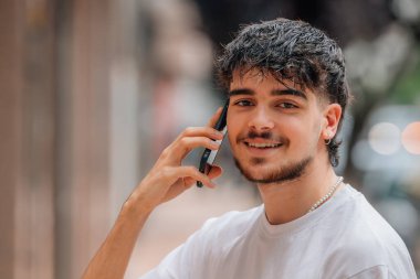 Sokakta cep telefonuyla konuşan genç bir erkek portresi.