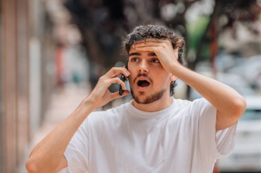 Sokakta cep telefonuyla konuşan genç adam şaşırmış, şaşırmış ya da inançsız bir ifadeyle.