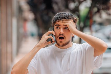 Sokakta cep telefonuyla konuşan genç adam şaşırmış, şaşırmış ya da inançsız bir ifadeyle.