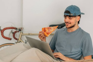 Bilgisayar başında pizza yiyen öğrenci ya da genç adam.