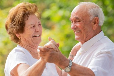 Gülümseyen yaşlı çift dışarıda mutlu bir şekilde dans ediyor.