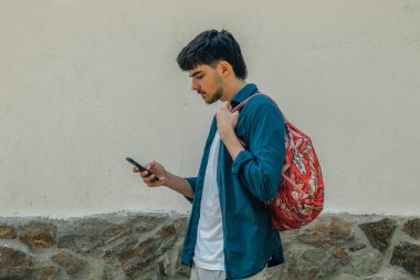 Sırt çantası ve cep telefonu olan genç ya da genç bir adam.
