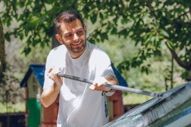 Genç adam dışarıda arabayı yıkıyor.