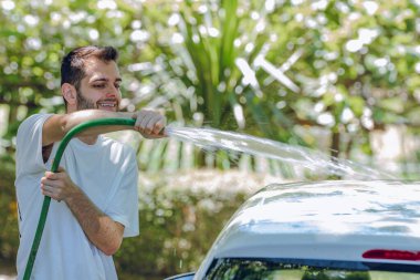 Genç adam dışarıda arabayı yıkıyor.