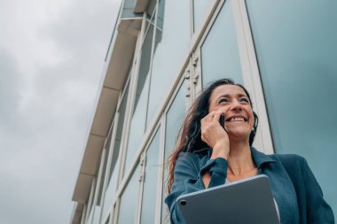 Tabletli iş kadını dışarıda cep telefonuyla konuşuyor.