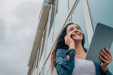 Tabletli iş kadını dışarıda cep telefonuyla konuşuyor.