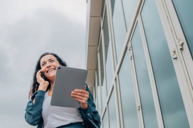 Tabletli iş kadını dışarıda cep telefonuyla konuşuyor.