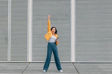 Heyecanlı bir kadın cep telefonuyla sokaklarda keyif çatıyor.