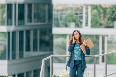 Ofis geçmişi olan bir iş kadını sokakta cep telefonuyla konuşuyor.
