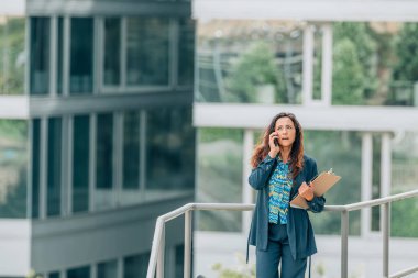 Ofis geçmişi olan bir iş kadını sokakta cep telefonuyla konuşuyor.