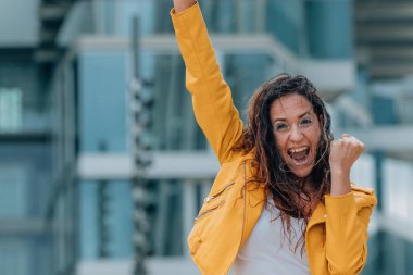 Başarı ve neşe dolu coşkulu ifadesiyle orta yaşlı bir kadın sokakta.