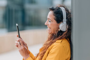 Cep telefonu ve kulaklığı olan orta yaşlı bir kadın.
