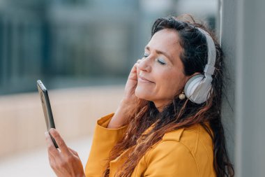 Cep telefonu ve kulaklığı olan orta yaşlı bir kadın.