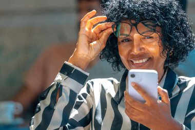 Cep telefonu ve gözlüklü orta yaşlı Latin kadın.