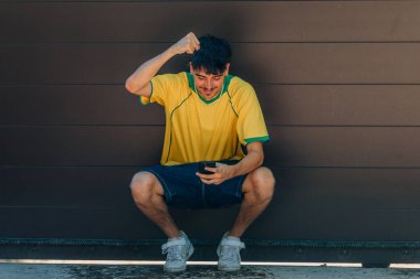 Cep telefonu ya da akıllı telefonu olan ve cep telefonuna bakan sarı tişörtlü genç adam.