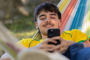 Hamaktaki cep telefonlu genç erkek.