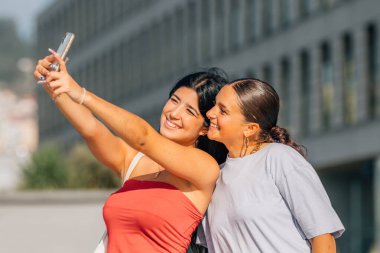 Kızlar sokakta cep telefonu kaydıyla eğleniyorlar ya da selfie çekiyorlar.